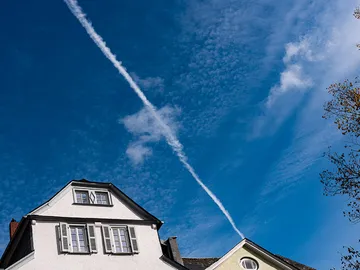 Ein Haus mit Wolken und einem Kondensstreifen am Himmel.