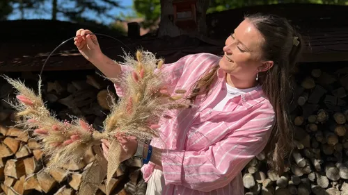 Frau hält Kranz im Freien bei Holzstapel.