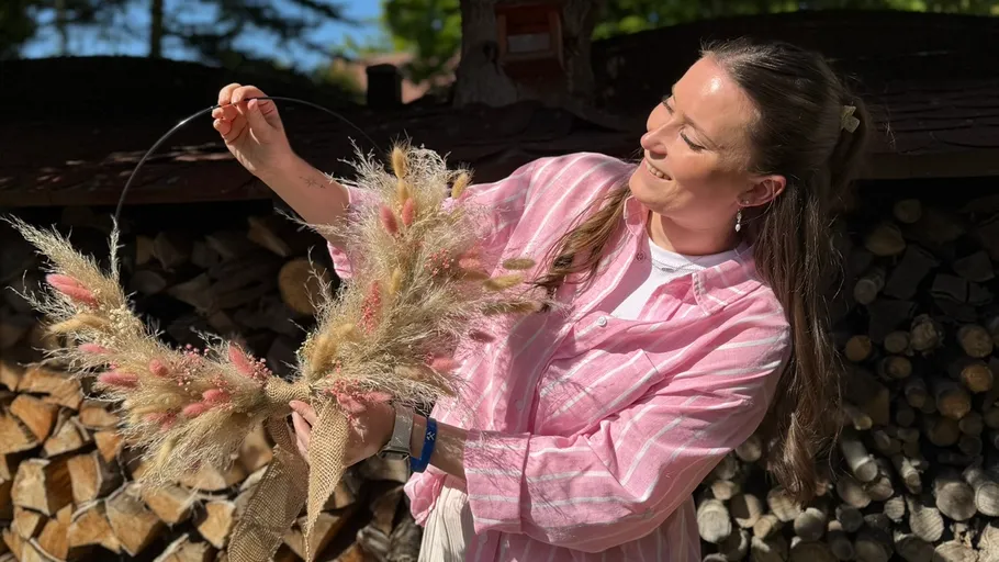 Frau hält Kranz im Freien bei Holzstapel.