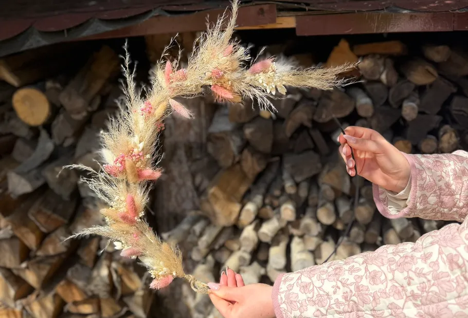 Hand hält Blumengesteck vor Holzscheiten.