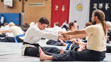 Two men practicing martial arts stretching indoors.