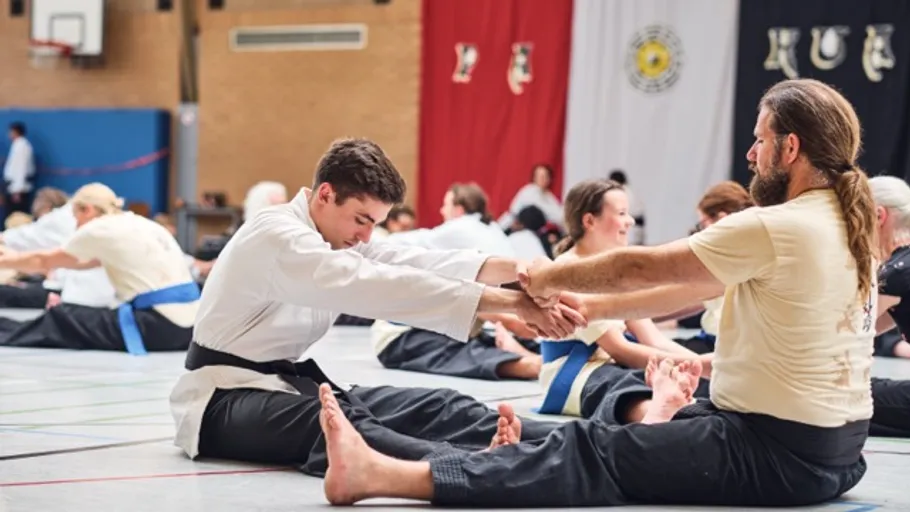 Two men practicing martial arts stretching indoors.