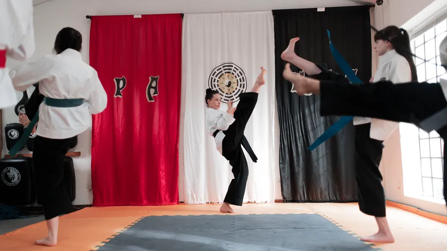 Martial artists practicing high kicks indoors.