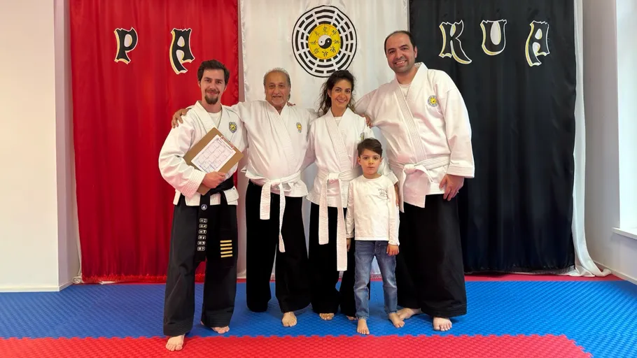 Five people in martial arts uniforms, dojo setting.