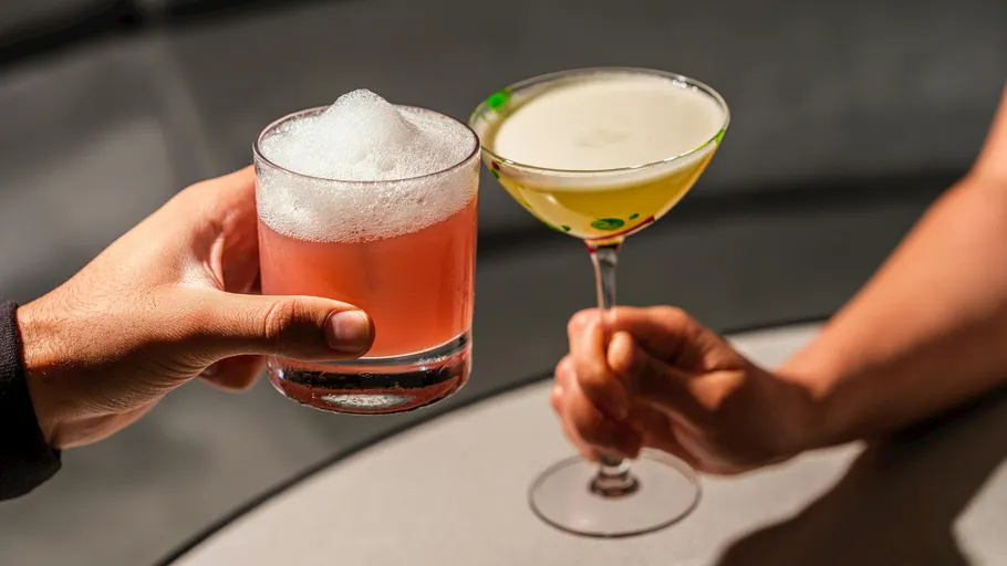 Two hands toasting with cocktails indoors.