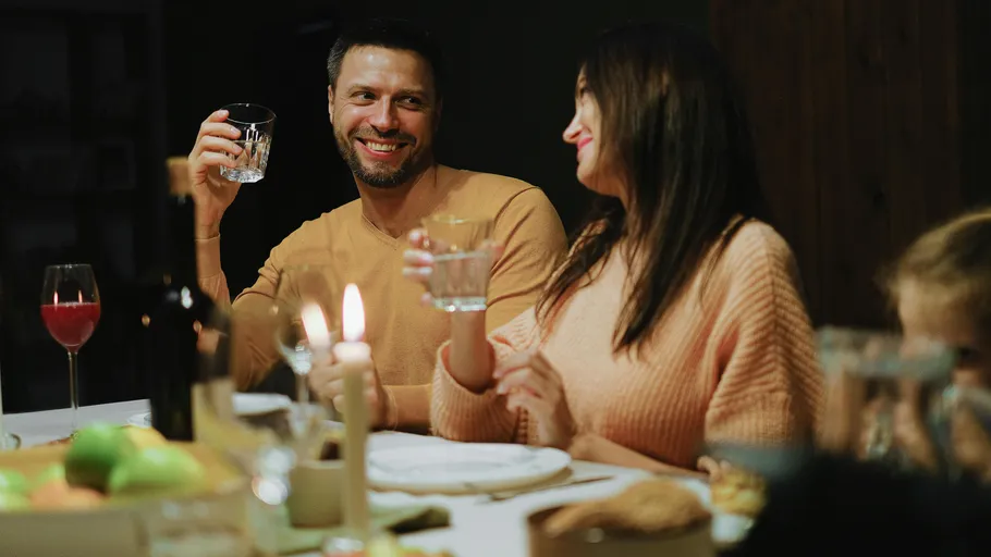 People smiling, holding drinks at dinner table.