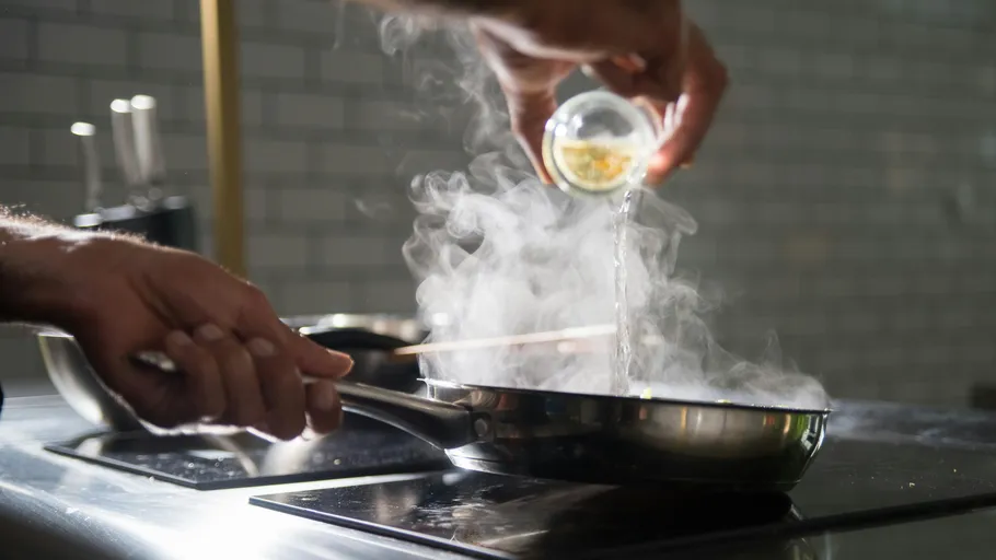 Person adding liquid to steaming pan.