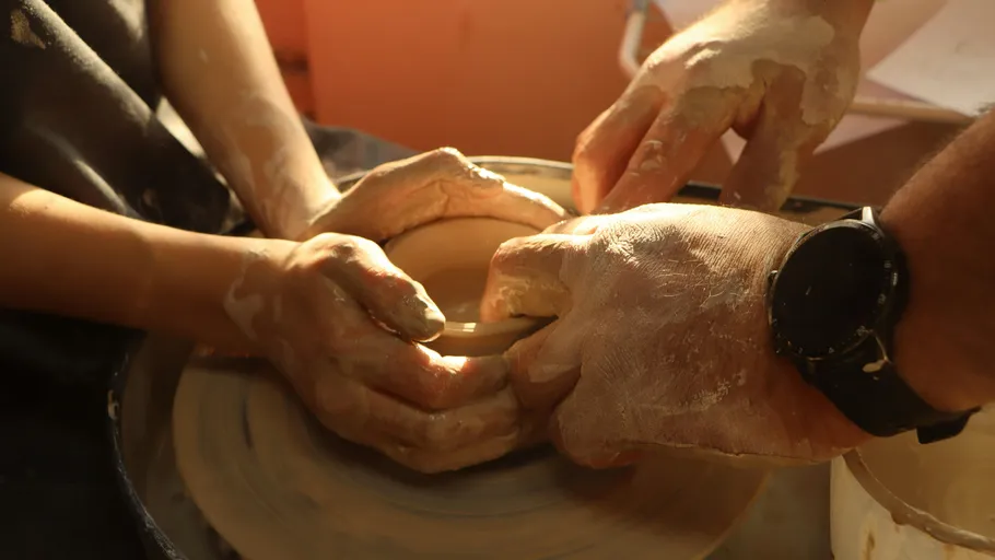 Hands shaping clay on pottery wheel.