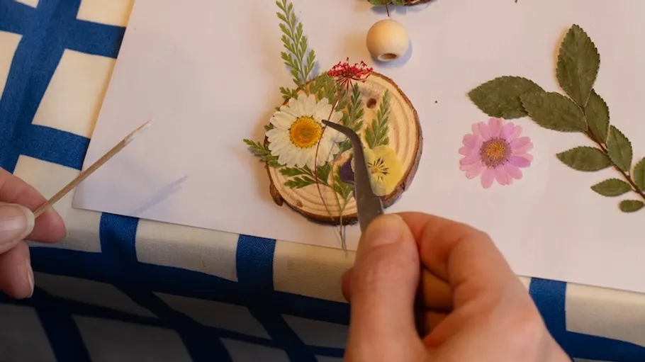 Hände basteln Blumen-Collage auf Holzscheibe.