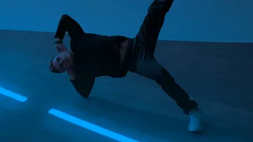 Man posing sideways in blue-lit room.