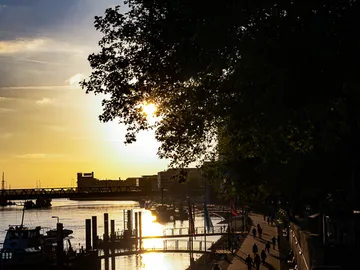 Sonnenuntergang über einem Fluss mit Spaziergängern und Bäumen.