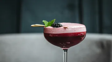 Lila Cocktail mit Schaum und Brombeergarnitur.