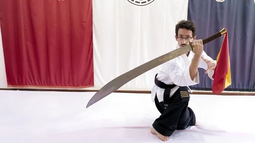 Martial artist kneeling with a large sword indoors.