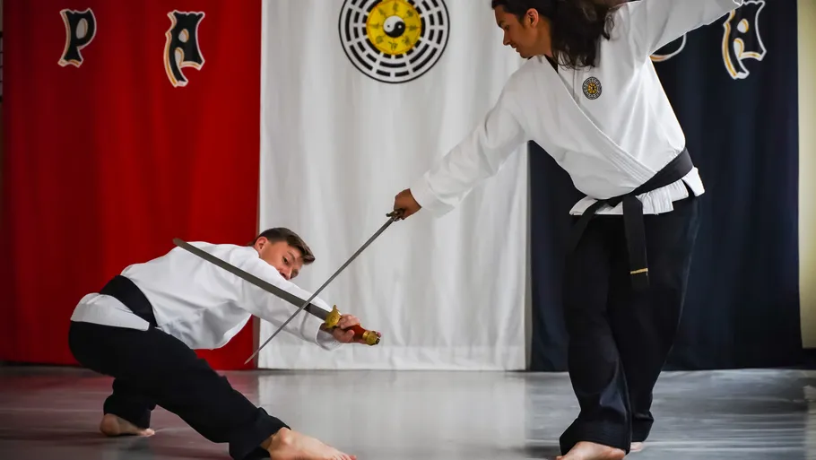 Two martial artists sword-fighting indoors.