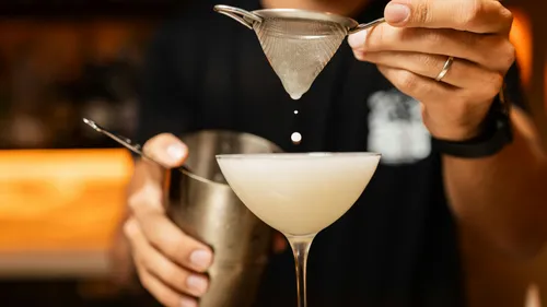 Bartender straining cocktail into glass at bar.