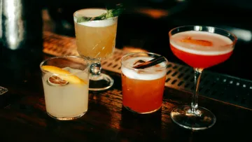 Four cocktails on a wooden bar counter.