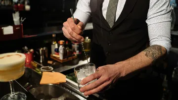 Bartender stirring drink with ice in bar.