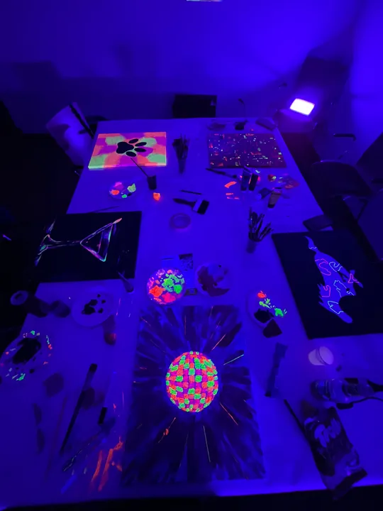 Neonbemalte Leinwand leuchtet unter Schwarzlicht im dunklen Raum.