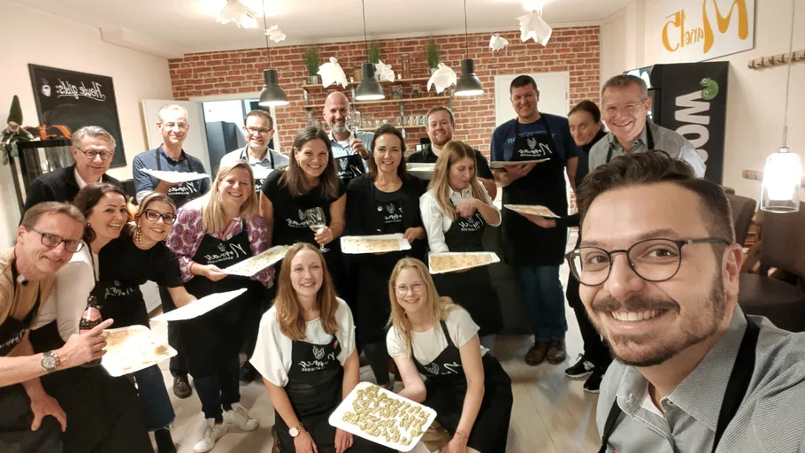 Group posing with homemade pasta in kitchen.