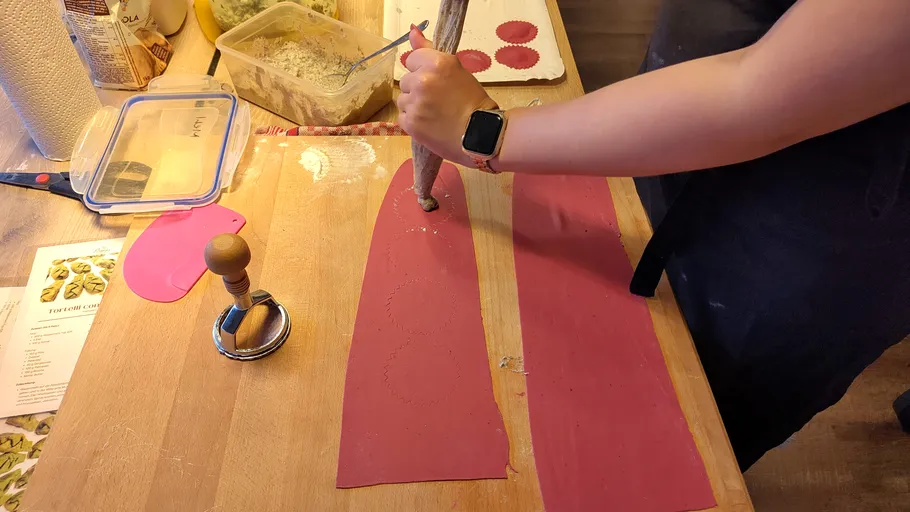 Person using piping bag on pink pasta dough.