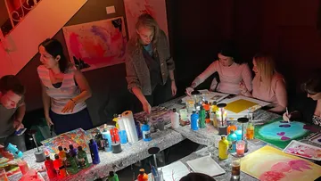 Personen malen an einem Tisch im dunklen Raum.