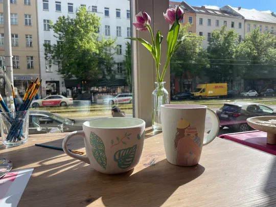 Two mugs and flowers on a sunny windowsill.