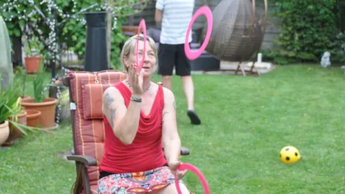 Woman sitting, juggling rings in a garden.