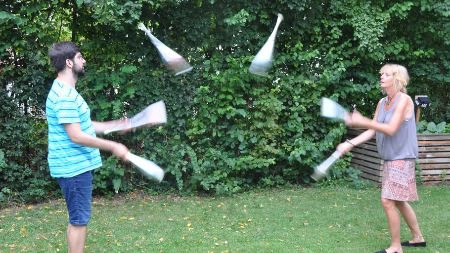 Zwei Personen jonglieren Keulen im Freien.