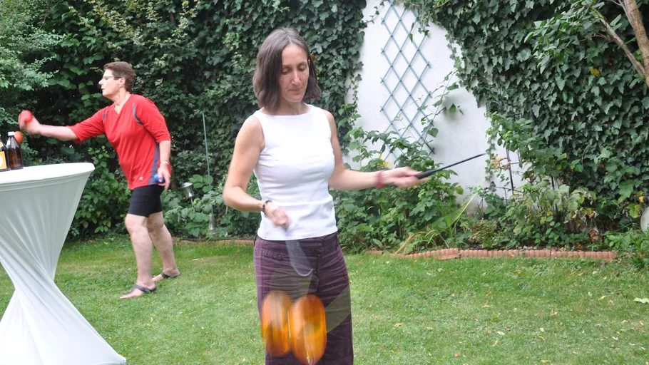 Woman spinning poi in a garden setting.