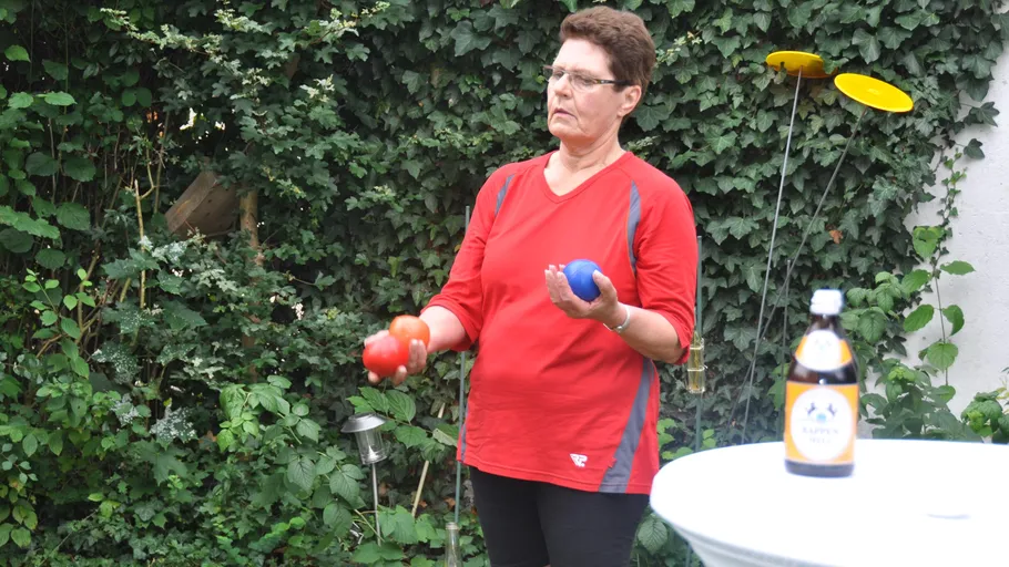 Person holds juggling balls in a garden.
