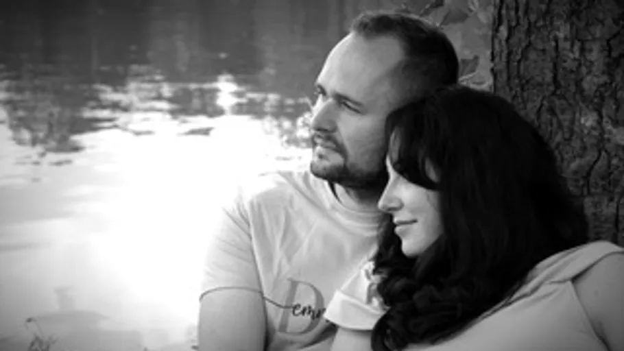 Couple sitting by a tree near water.