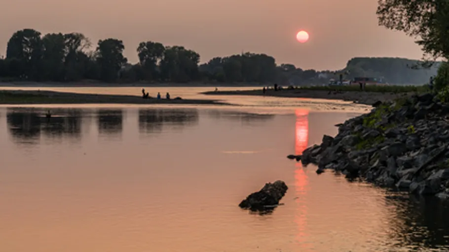 Sunset over river with silhouettes of people.