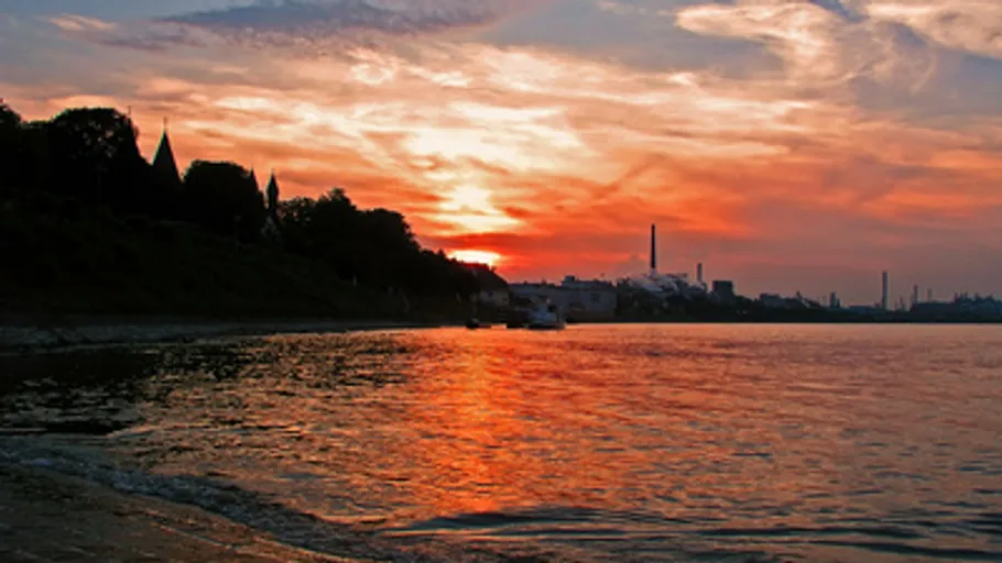 Sonnenuntergang über Fluss mit Industriehorizont.