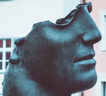Bronze sculpture of a head, partially damaged, outdoors.