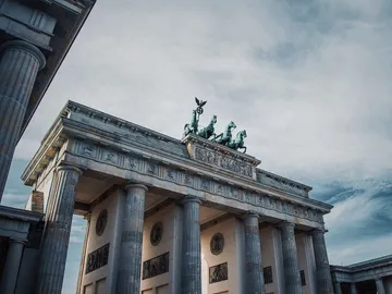 Tor mit Säulen, oben Pferde, vor bewölktem Himmel.