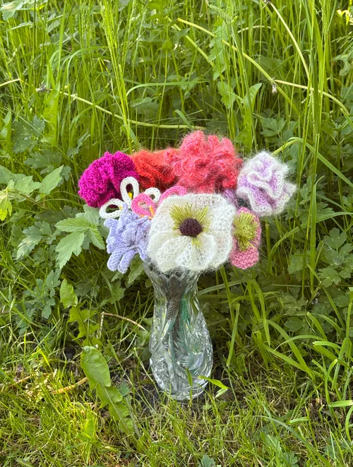 Gestrickte Blumen in Vase auf Gras.