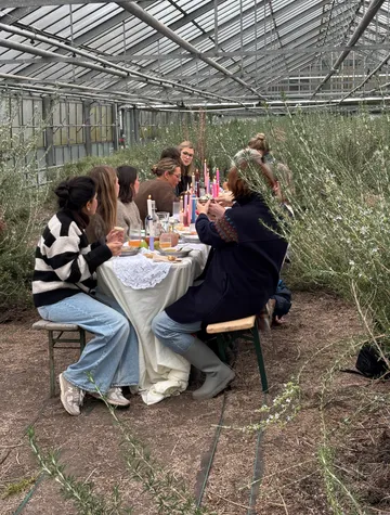 Personen essen an Tisch im Gewächshaus.