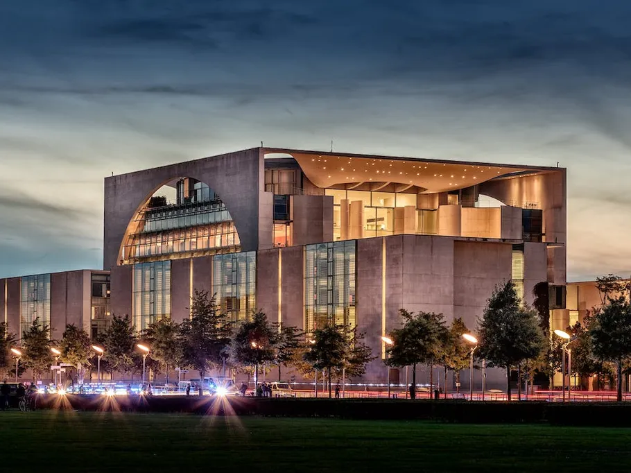 Modern government buildings glow in the evening, surrounded by trees.