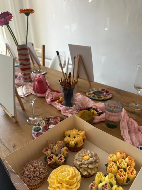 Cupcakes und Malutensilien auf dekoriertem Tisch.