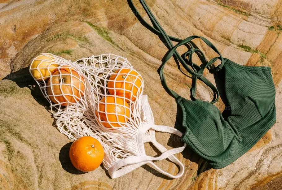 Netztasche mit Früchten, Bikini auf Felsen.