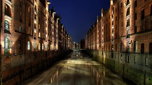 Historische Backsteinlager nachts beleuchtet, spiegeln im Wasser.