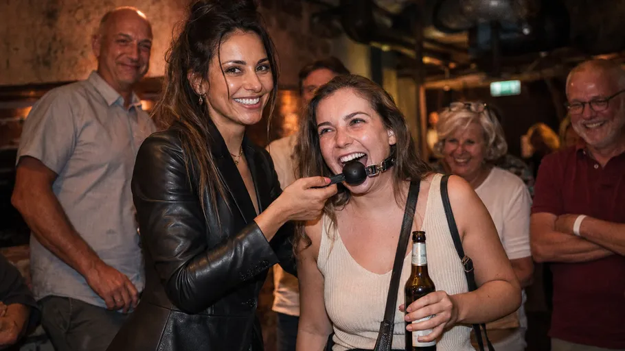 Zwei lachende Frauen, eine hält eine Flasche.