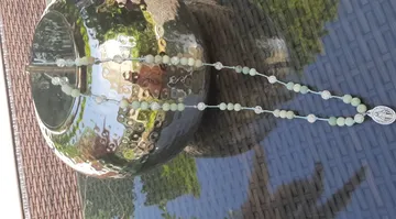 Rosary with beads on reflective vase outside.