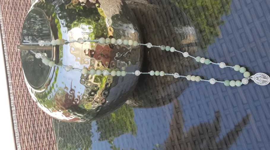 Rosary with beads on reflective vase outside.