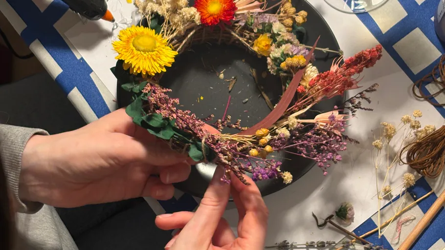 Hände fertigen Blumenkranz auf schwarzem Teller.