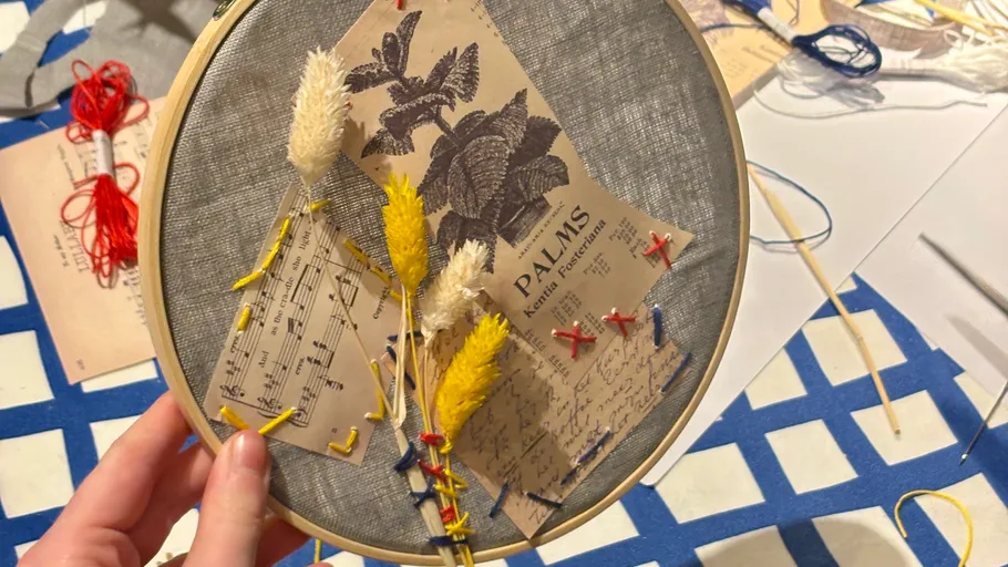 Hand holding embroidery hoop with dried flowers.