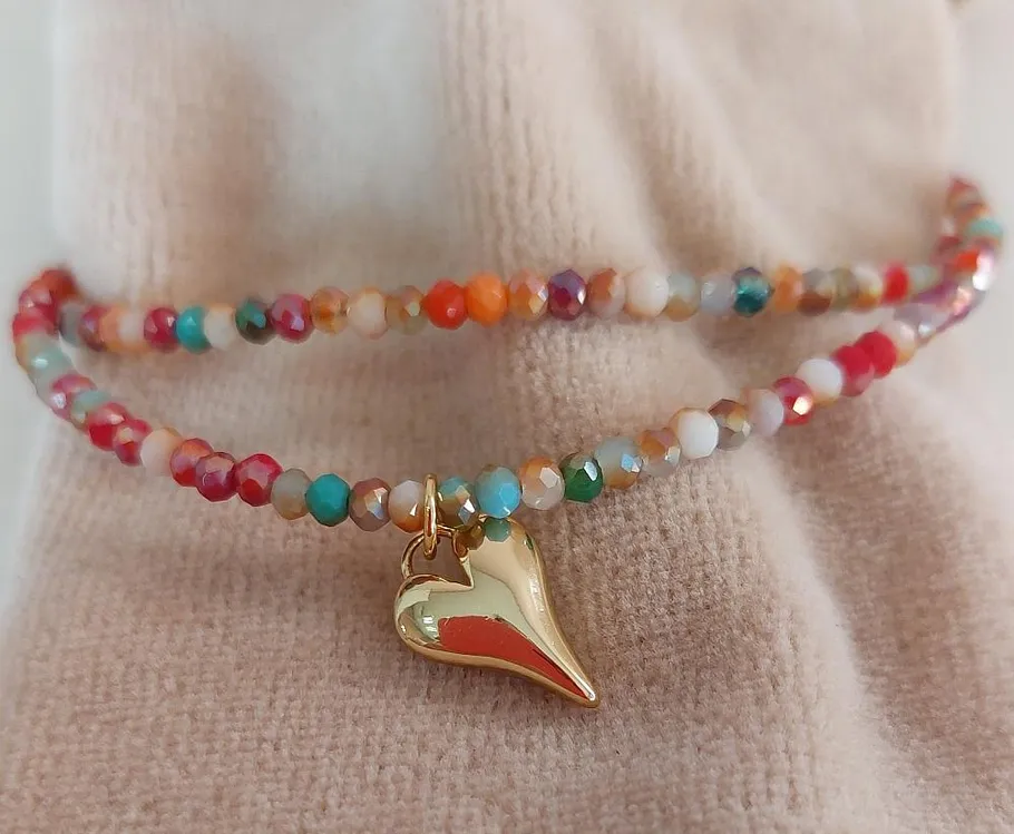 Buntes Perlenarmband mit Herzanhänger auf Stoff.