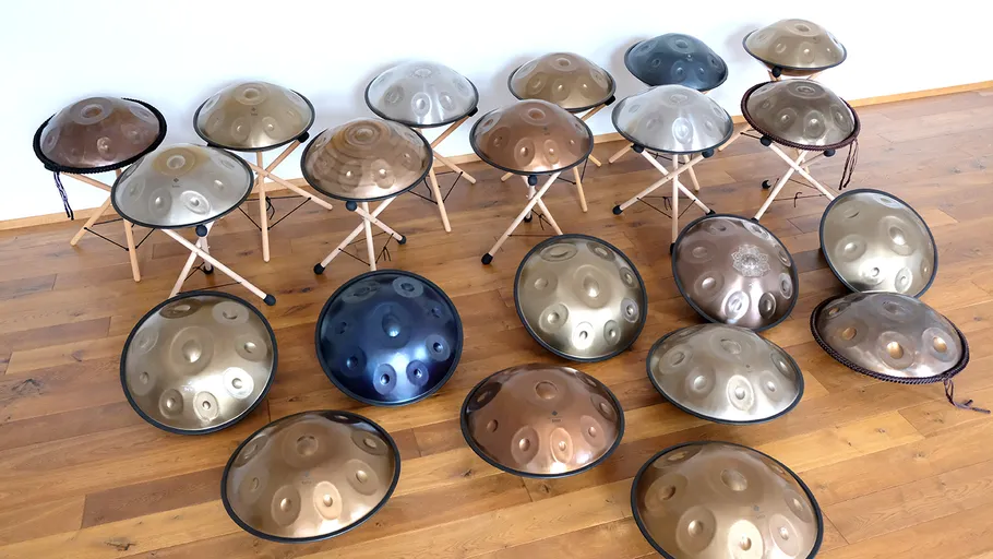 Multiple handpans displayed on wooden floor and stands.