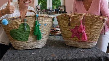 Two women display decorated woven baskets indoors.