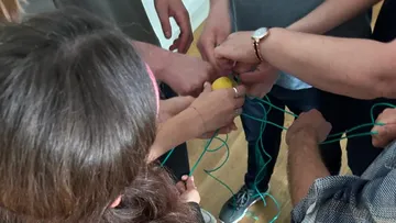 Group holding strings connected to a lemon indoors.